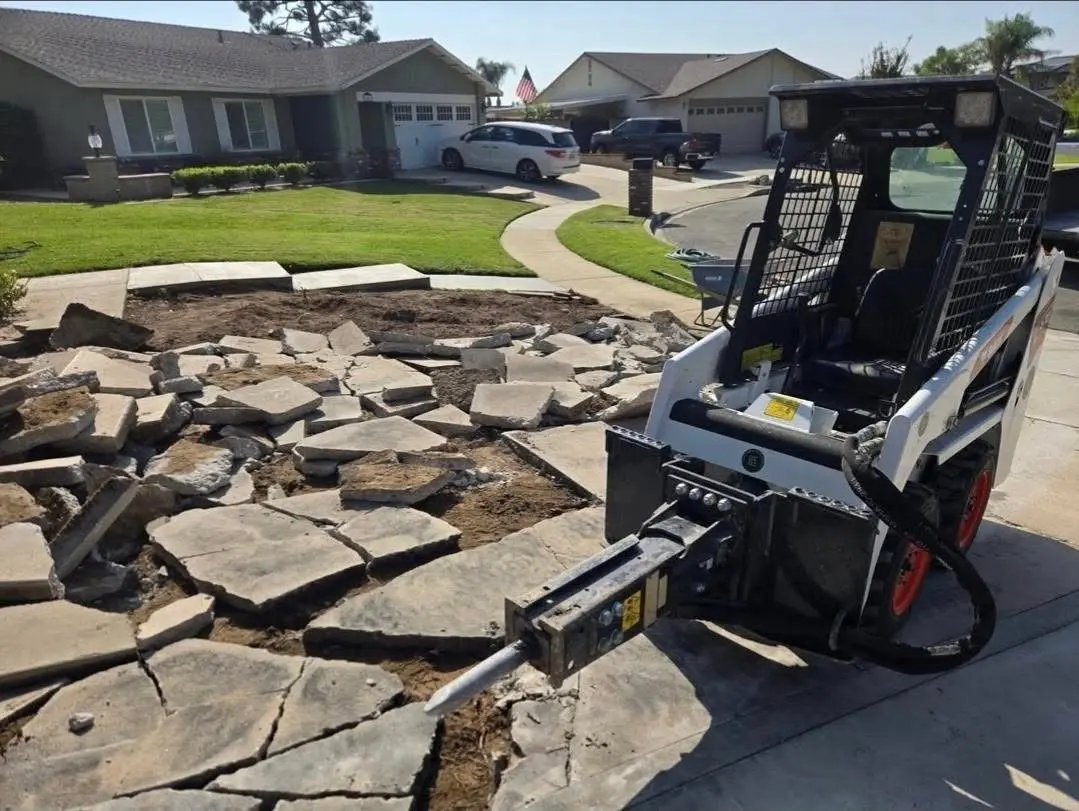 Skid steer with hydraulic breaker removing an existing concrete patio