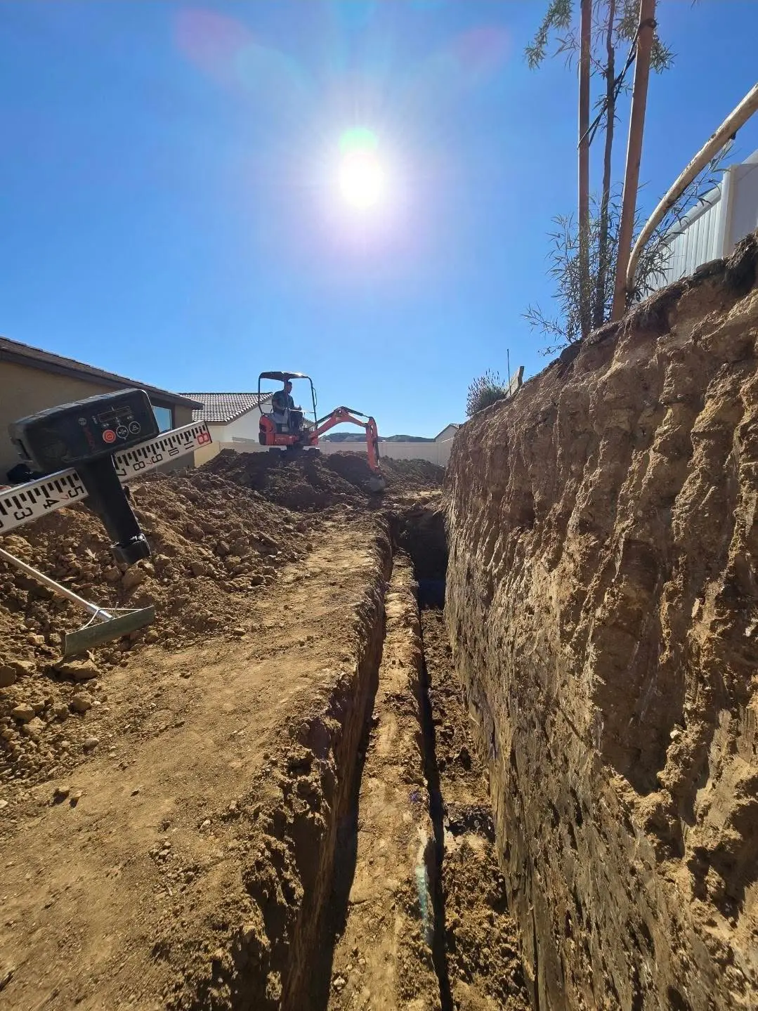 Compact excavator completing deep excavation and trench work on a residential property