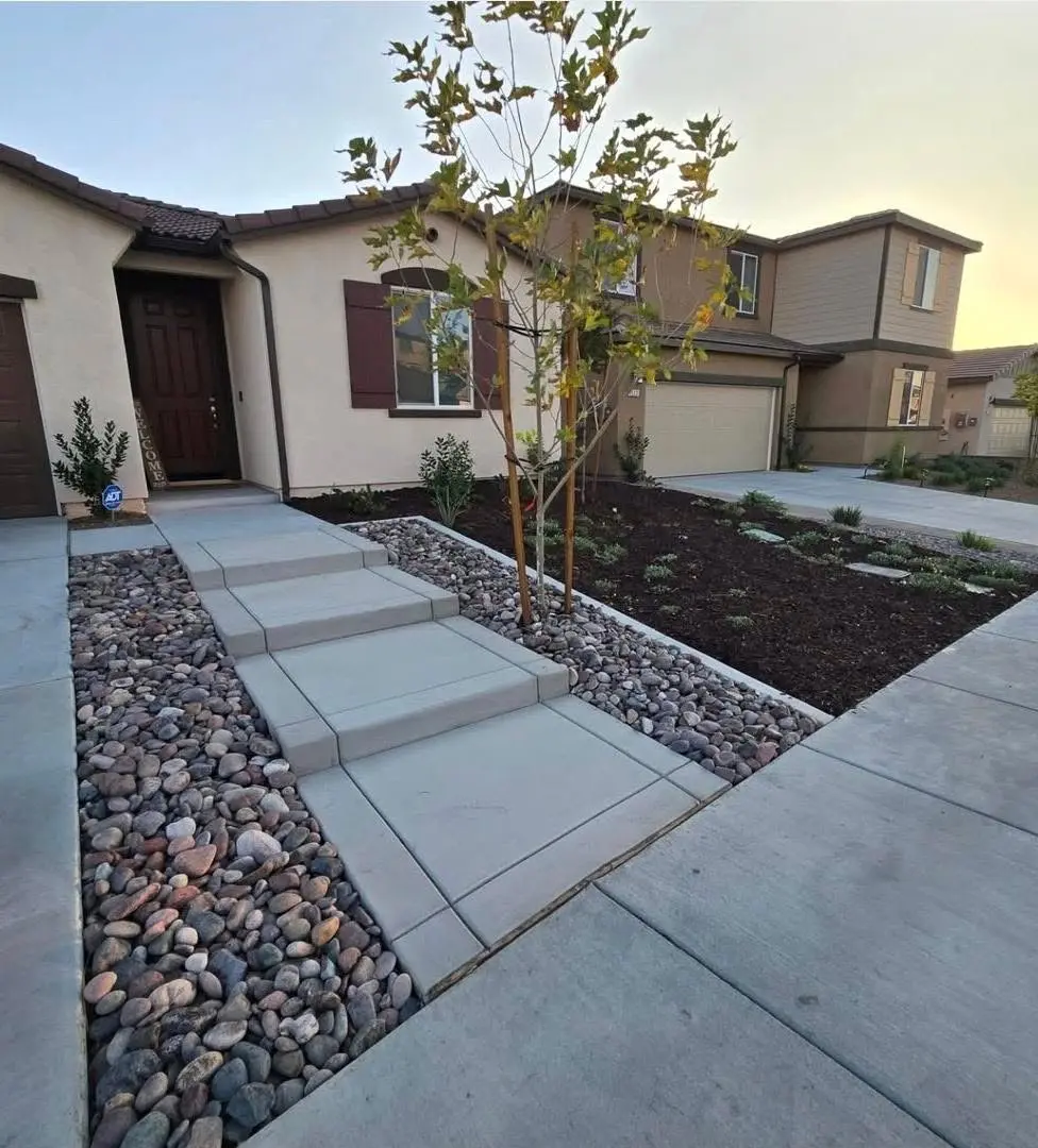 Finished front-yard concrete walkway with decorative river rock and new landscaping